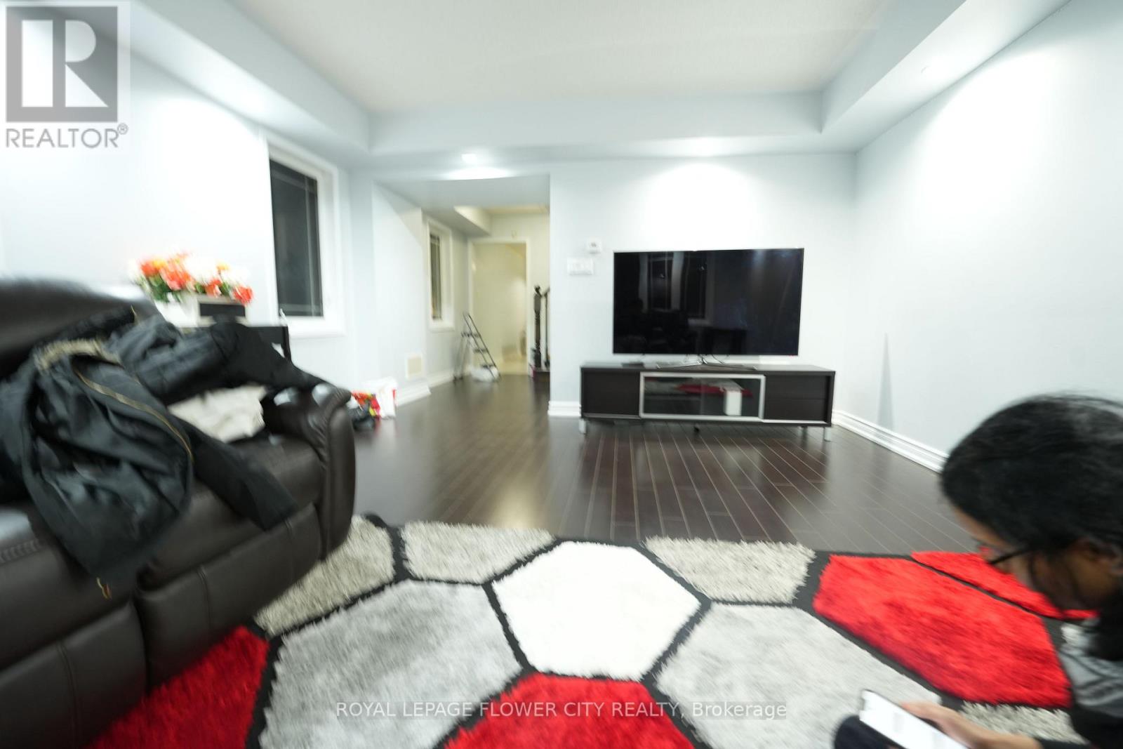 A man is sitting on a black leather couch in a living room with a red and black rug.