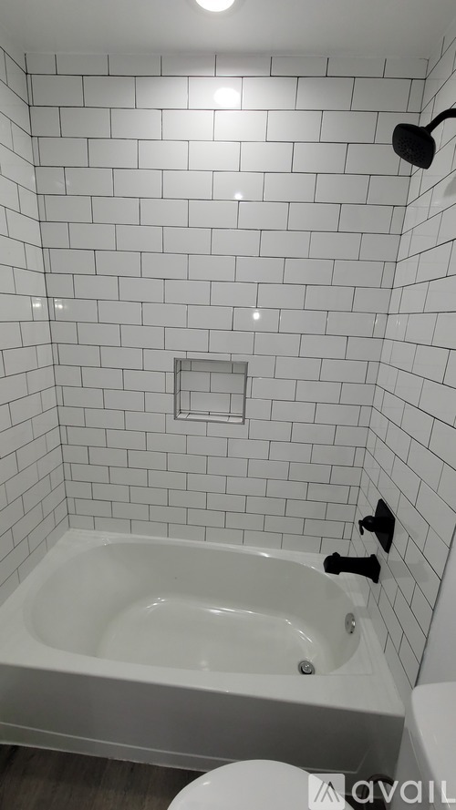 A white tiled bathroom with a white bathtub and toilet.