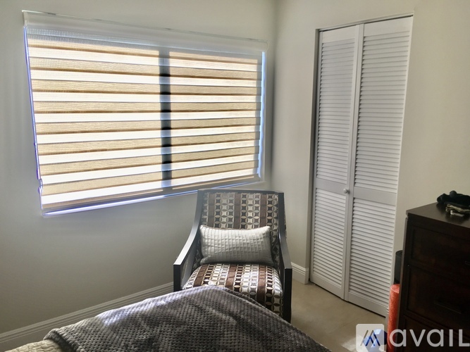 A bedroom with a bed, chair, and window with blinds.