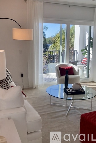 A living room with a white couch, a glass table, and a red chair.