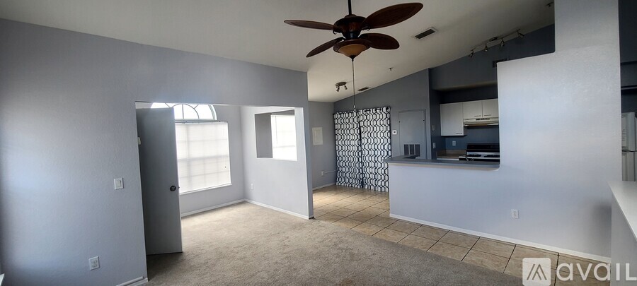 A living room with a ceiling fan and a kitchen area in the background.