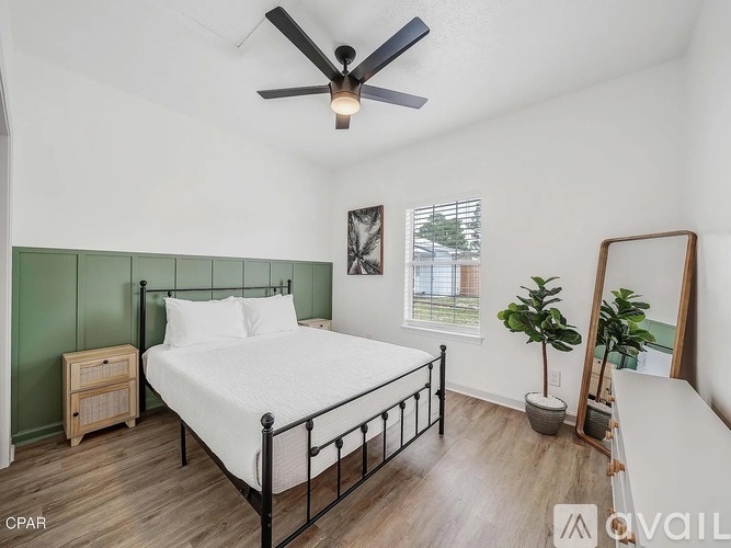A bedroom with a bed, a dresser, a plant, and a mirror.