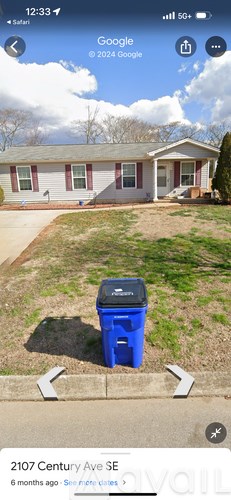 A blue trash can is in front of a house.