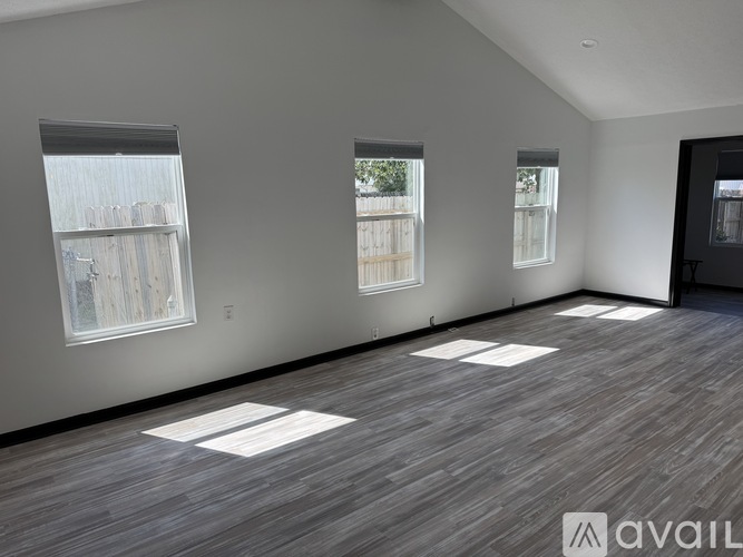 A room with wooden flooring and three windows.