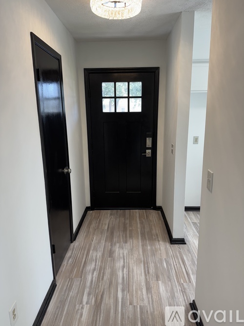 A hallway with a black door and wooden flooring.