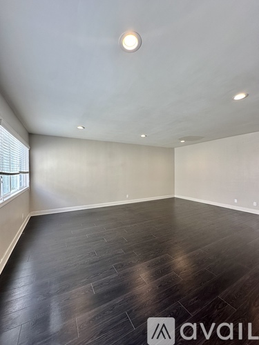 A room with wooden flooring and a window on the left side.