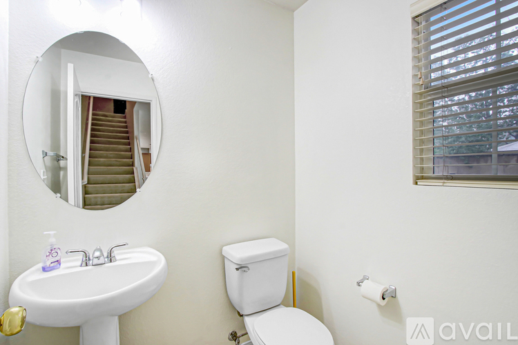 A bathroom with a white sink, toilet and a round mirror.