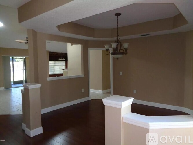A room with a brown floor and tan walls with a chandelier hanging from the ceiling.