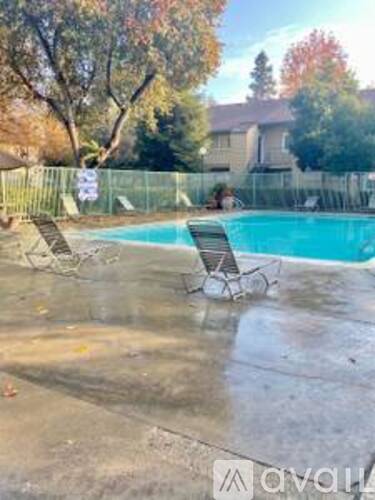 A pool with two chairs and a fence in the background.