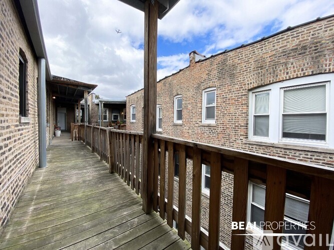 A wooden deck leads to a brick building with a balcony.