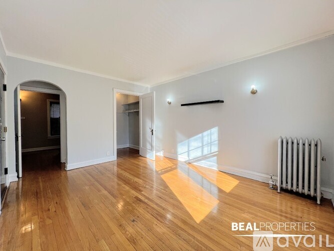 A spacious room with wooden floors and white walls, with a radiator on the right side.