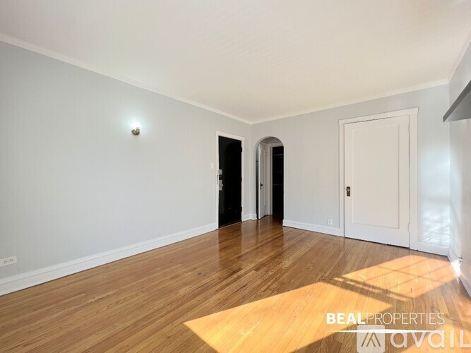 A room with wooden flooring and white walls, with a door on the right and a window on the left.