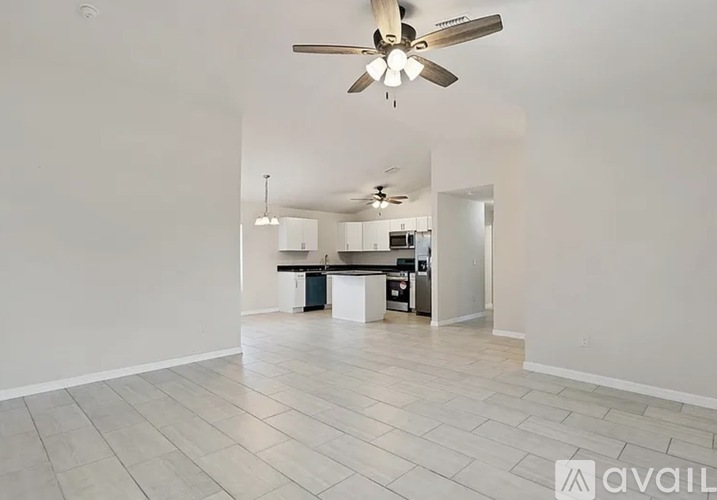 A spacious room with a ceiling fan and a kitchen area in the background.