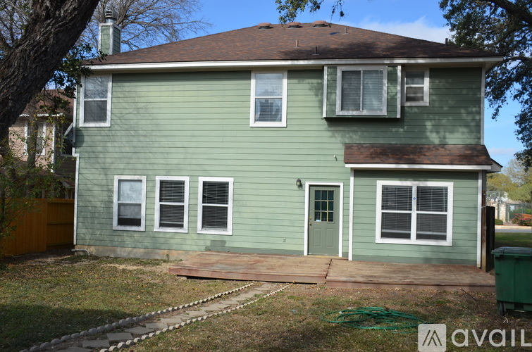 A green house with a brown roof and a green trash can in front.