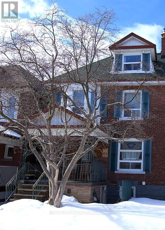 A large tree in front of a two-story house with snow on the ground.