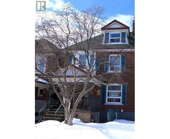 A large tree in front of a two-story house with snow on the ground.