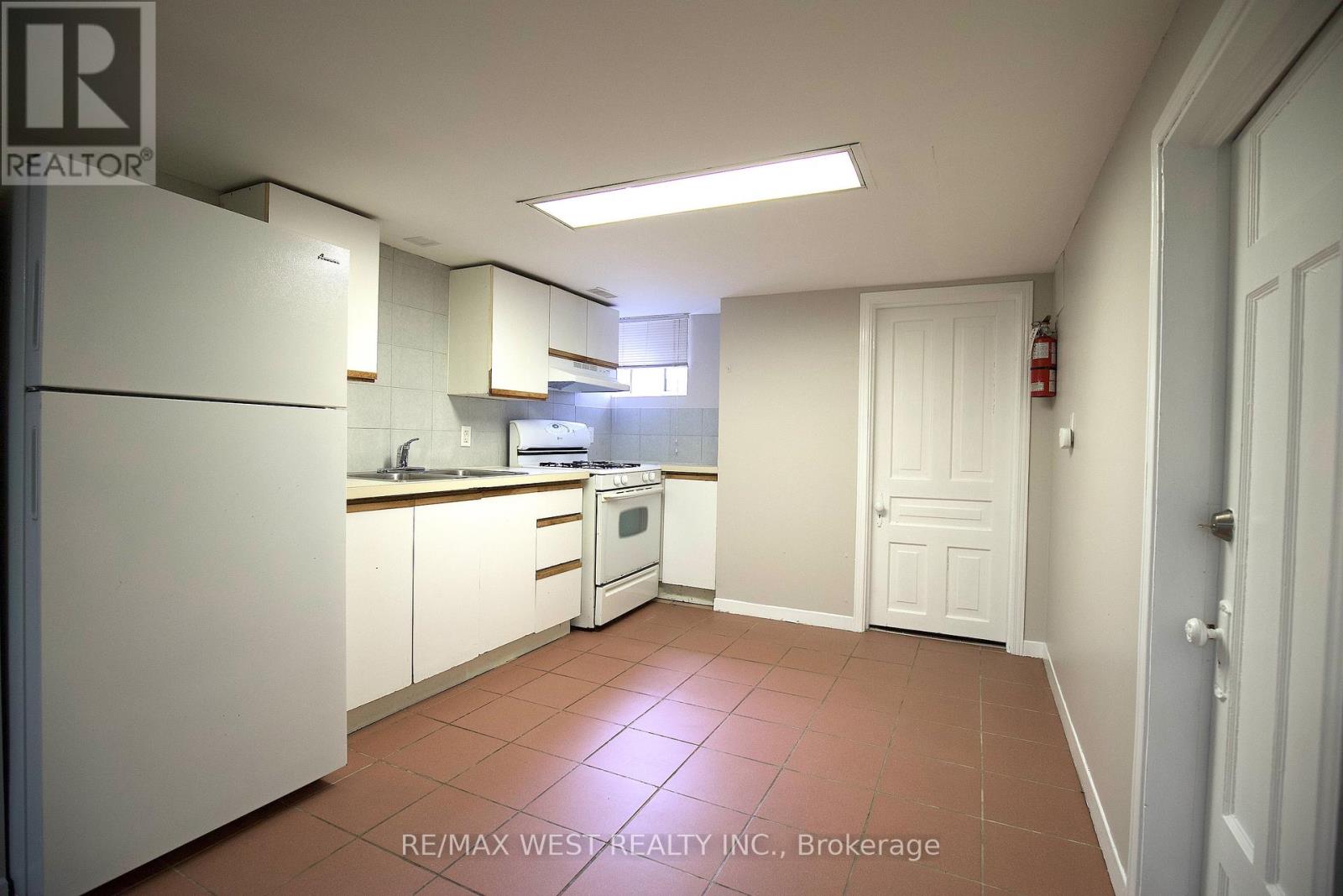 A kitchen with white appliances and brown tile flooring.