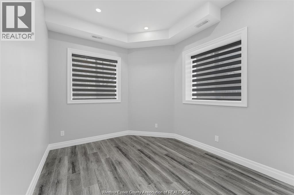 A room with wooden flooring and two windows with blinds.