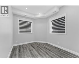 A room with wooden flooring and two windows with blinds.