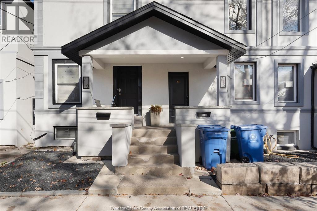 A house with a black front door and two blue bins in front.