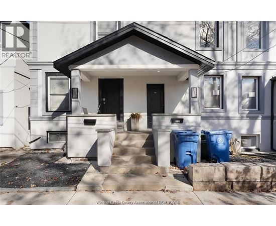 A house with a black front door and two blue bins in front.