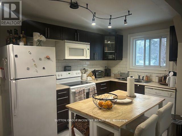 A kitchen with a white fridge and a wooden table with a bowl of fruit on it.