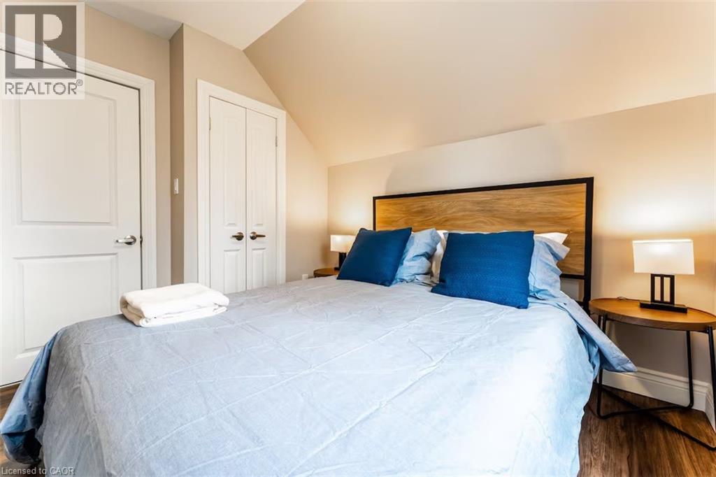 A bedroom with a bed, two pillows, a nightstand with a lamp, and a wall-mounted light fixture.