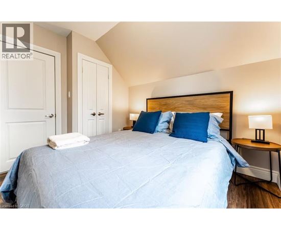 A bedroom with a bed, two pillows, a nightstand with a lamp, and a wall-mounted light fixture.
