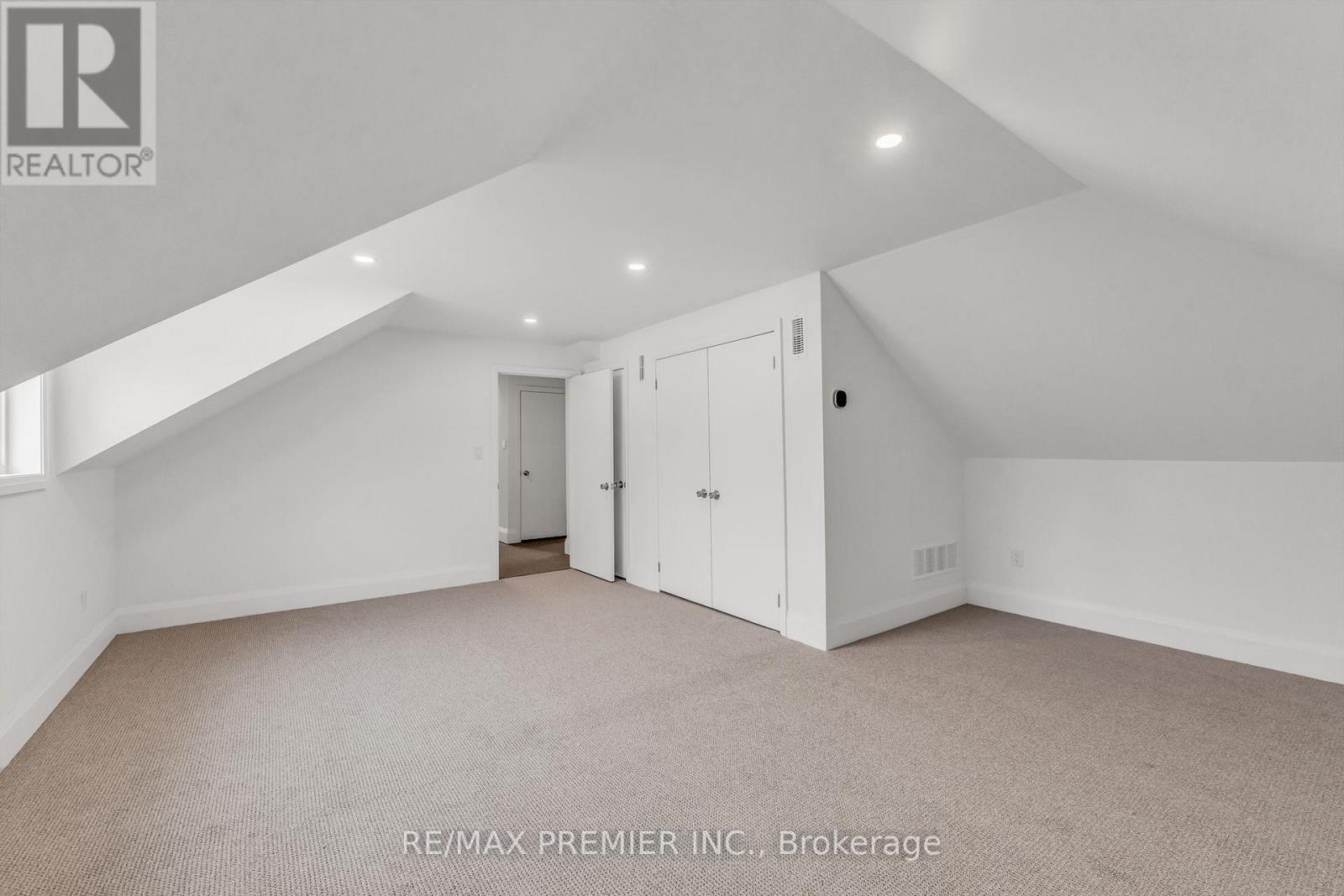 A spacious room with a carpeted floor and white walls, with a door on the right and a window on the left.