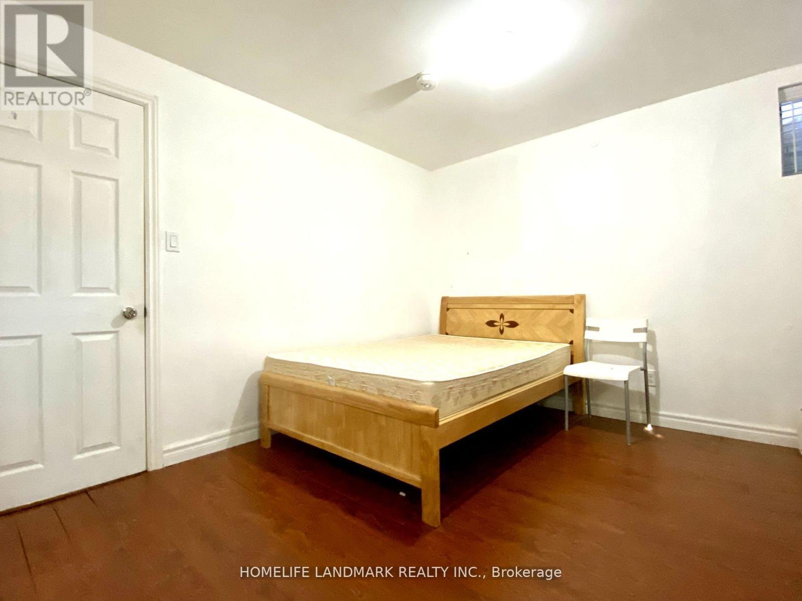 A bedroom with a bed, chair, and brokerage sign.