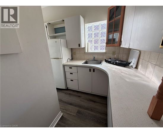 A kitchen with white cabinets and a window with a purple and white curtain.