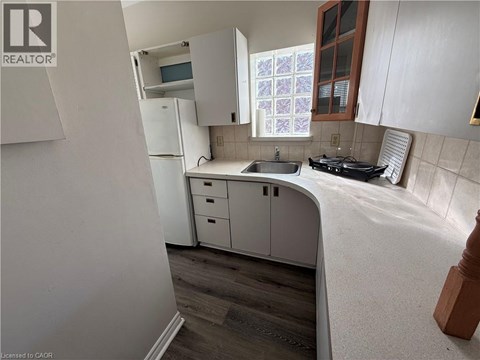 A kitchen with white cabinets and a window with a purple and white curtain.