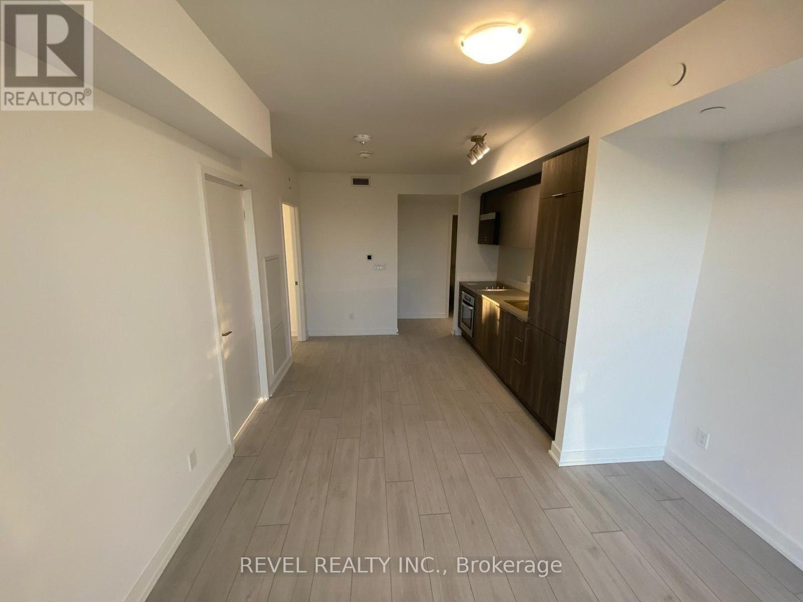 A long, empty hallway with a door on the left and a kitchen area on the right.