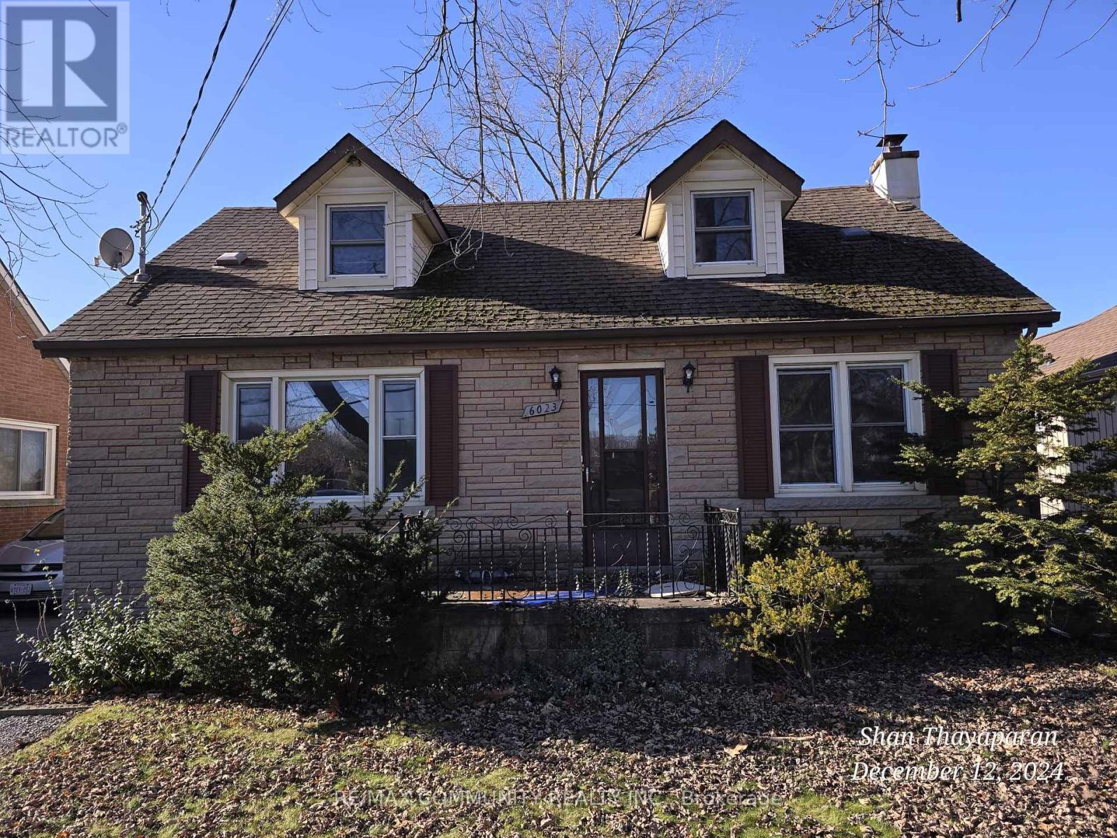 A house with a brown roof and a black door is surrounded by bushes and trees.