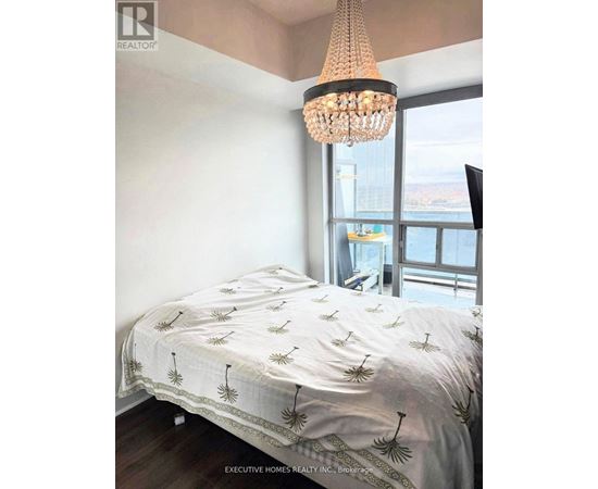 Bedroom with a bed covered in a white sheet with palm tree prints on it.