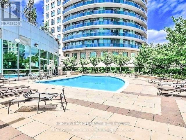 A swimming pool surrounded by lounge chairs in front of a multi-story building.