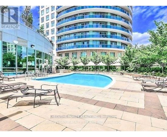 A swimming pool surrounded by lounge chairs in front of a multi-story building.