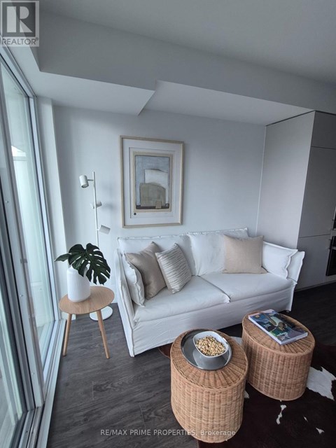 A living room with a white couch, a plant on a stool, and two wicker tables with bowls on them.