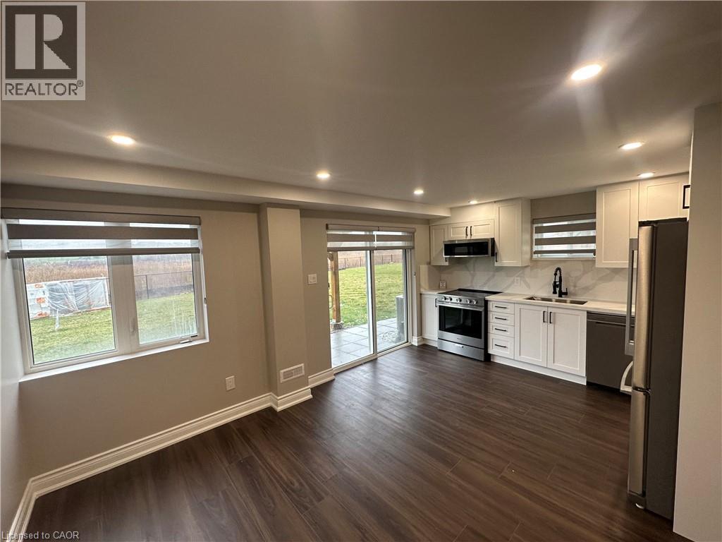 A well-lit, empty kitchen and living room with wooden floors and white cabinetry.