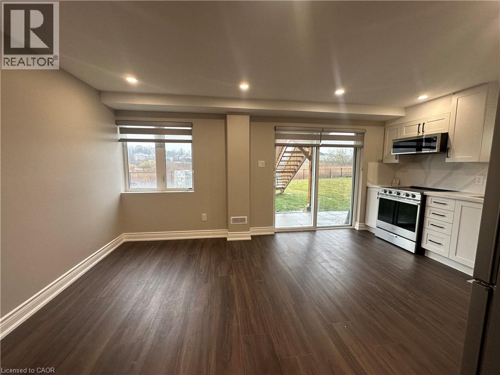 A well-lit, empty living room with wood flooring and a kitchen area in the background.