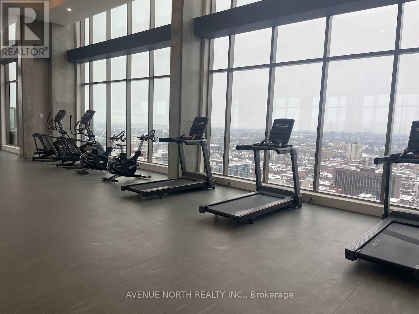 A gym with treadmills and exercise bikes in front of a large window overlooking a cityscape.