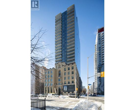 A tall building with a glass facade stands in front of a building with a beige facade.