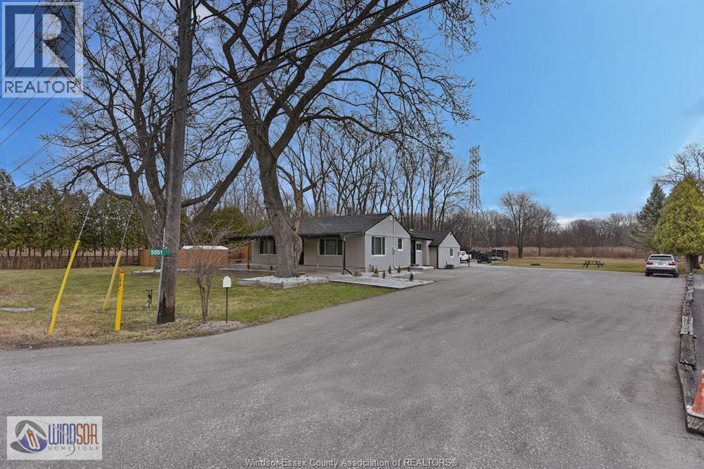 A real estate listing photo shows a house with a driveway and trees.