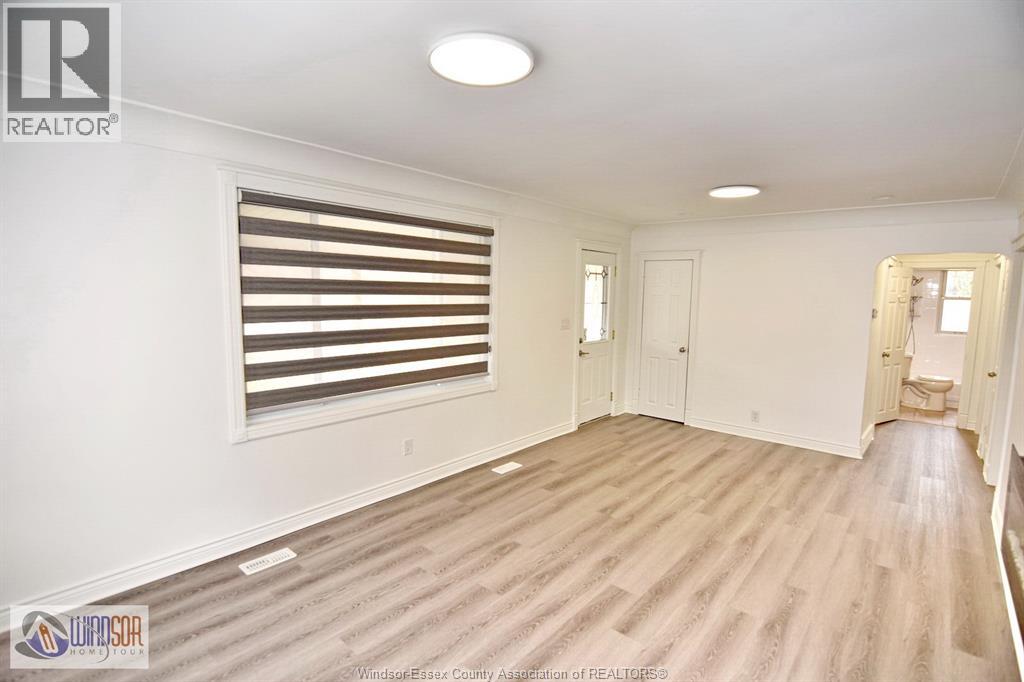 A spacious room with wooden flooring and a window with horizontal blinds.