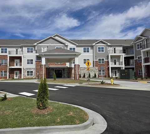 A yellow pedestrian crossing sign is in front of a large apartment building.