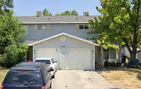 A blue car is parked in front of a house with a garage.