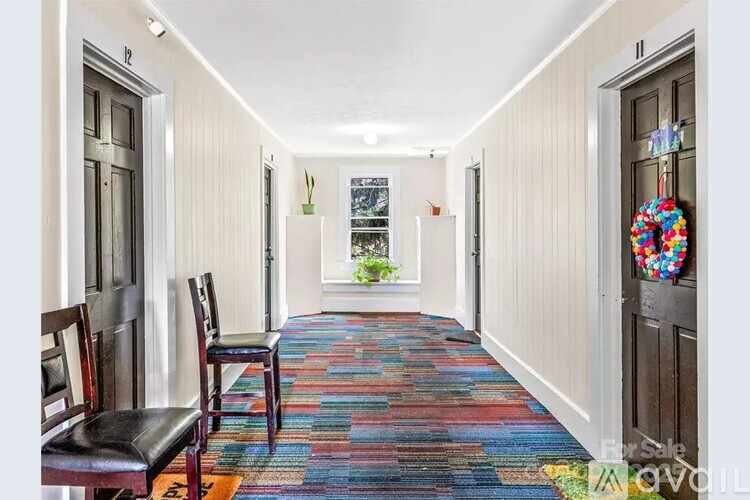 A hallway with a colorful carpet and two chairs on the left side.