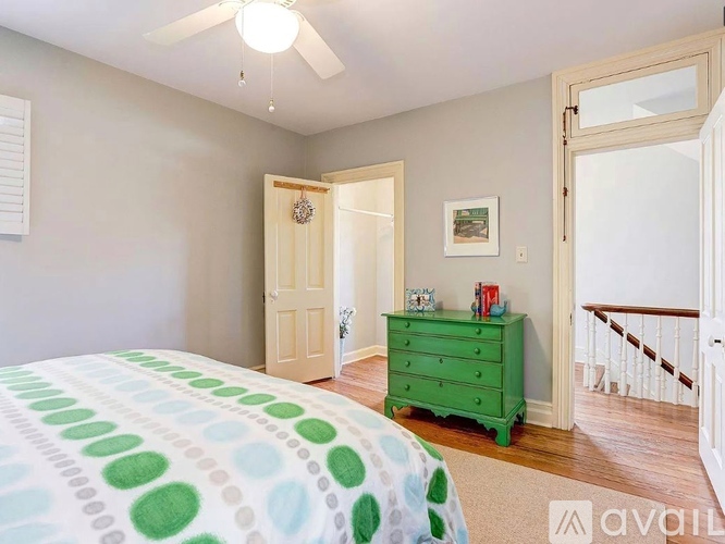 A bedroom with a green dresser and a bed with a green and white comforter.