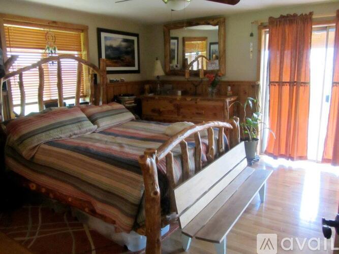 A bedroom with a bed, dresser, mirror, and window with orange curtains.