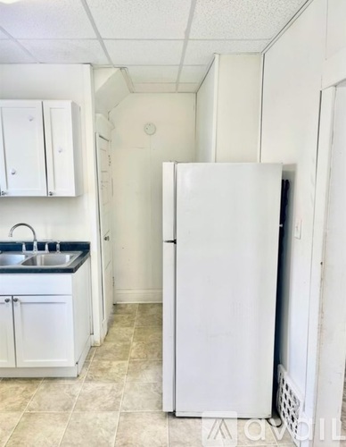 A white refrigerator is in a kitchen with white cabinets.